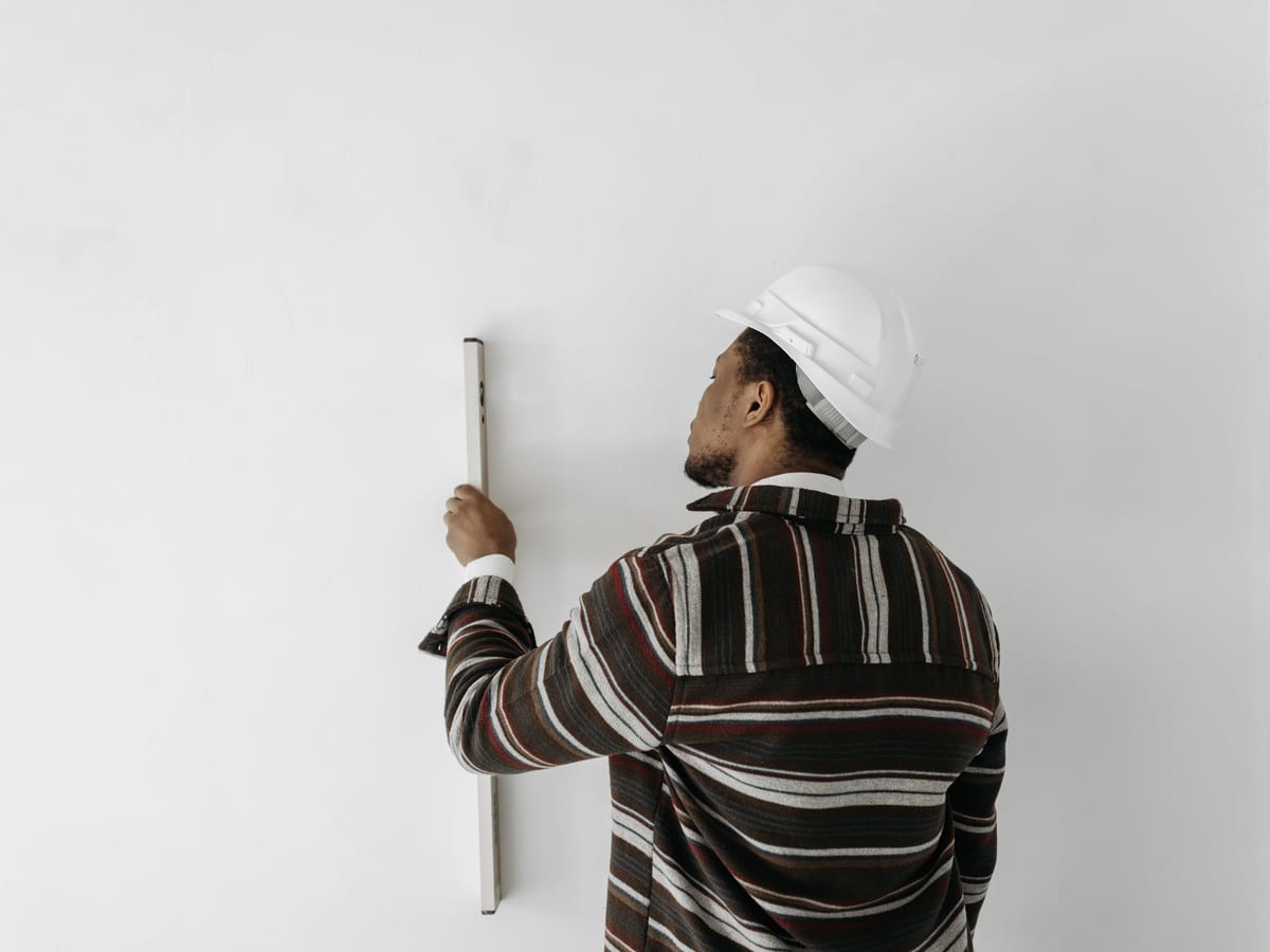 Back view of a man using a level to measure wall verticality indoors.
