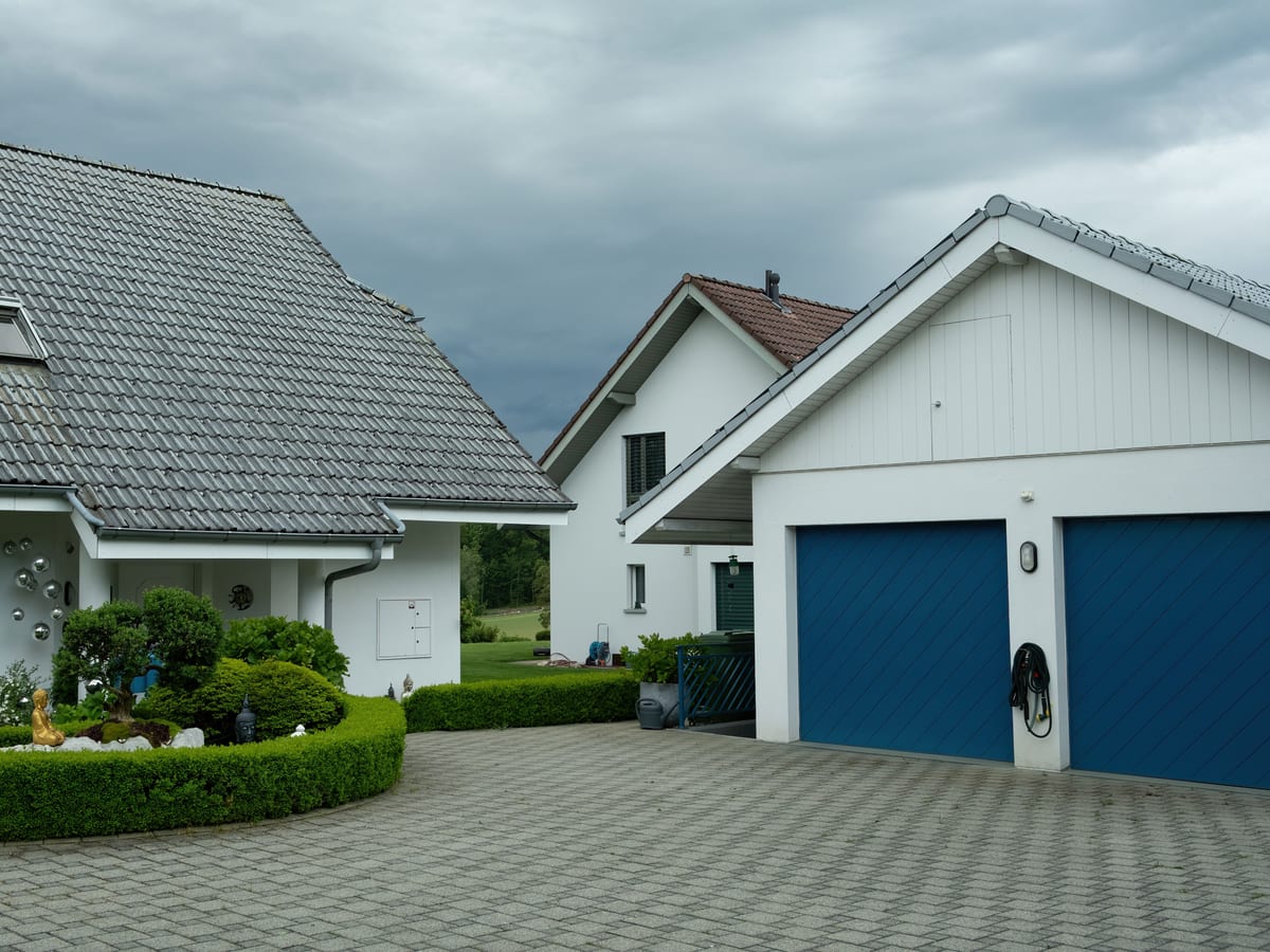 Lovely suburban houses with blue garage doors under cloudy sky, surrounded by greenery.