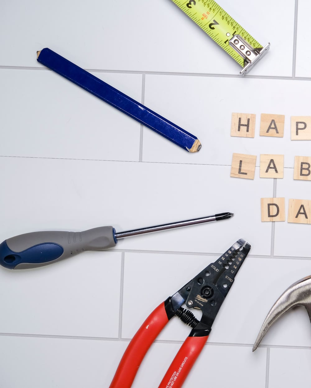 Flat lay of various tools surrounding 'Happy Labor Day' text on tiles.