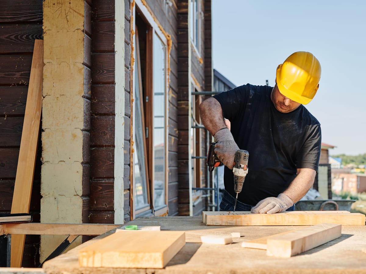 A construction worker using a power drill on a building site, outdoors during the day.